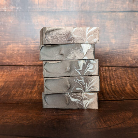 Five bars of grey soap, with a silver swirl on the tops, stacked one atop another.