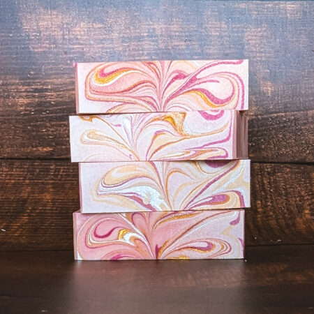 Four soap bars stacked on top of one another, showing off the gorgeous pink, white, and gold swirl on the top of the bars.
