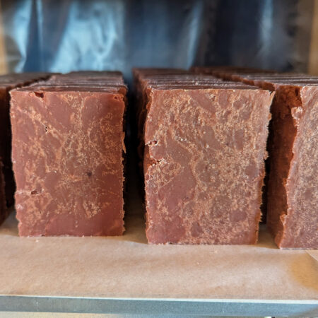 Deep Red Soaps sitting on their ends on the curing shelf. The patterning inside the bars is reminiscent of stonework, shot through with lighter and darker lines, but it's simply because this soap was very naughty and had to be shoved into its moulds.