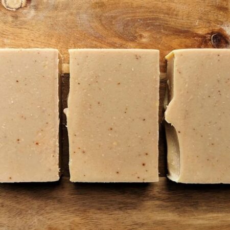 Myrrh and Orange Soap. Tan coloured soap bars set alongside each other and photographed on a wooden board. There are small dark specks in the soap.