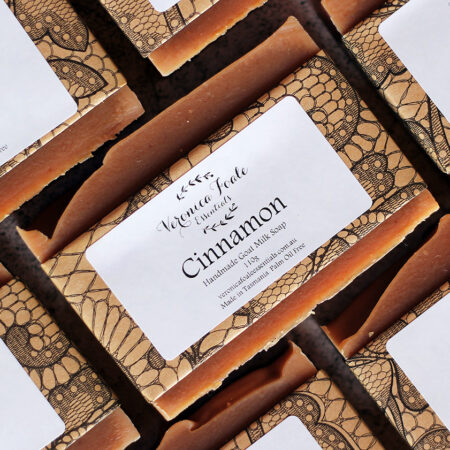 Warm brown bars of soap, packed in patterned brown and black paper, with white labels describing them as "Cinnamon Goat Milk Soap"