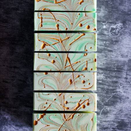 Bars of soap, photographed top down, all lined up. The soap is creamy green, with specks and flicks of gold mica in oil.