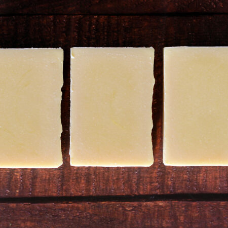 Three bars of pale yellow soap against a wooden background.