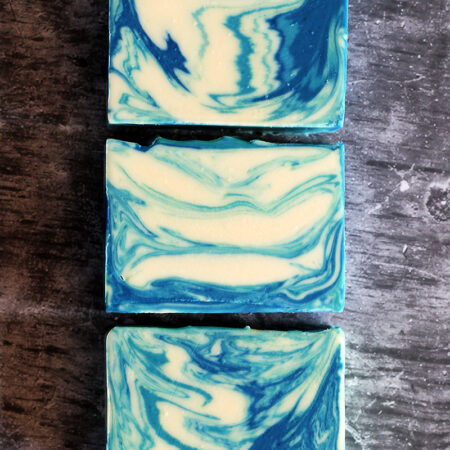 Three bars of soap laying flat so you can see the beautiful swirl inside. The soap is white, deeply blue, and deeply green swirled. It is gorgeous.