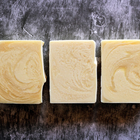 Three bars of soap against a stone like background. The soap is swirled, creamy white against slightly more yellow white.