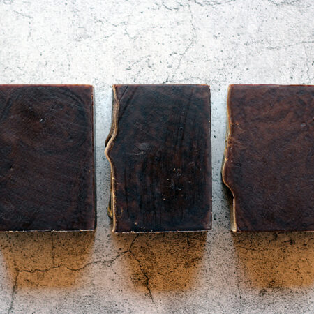 Three bars of very dark brown soap against a stone-like background