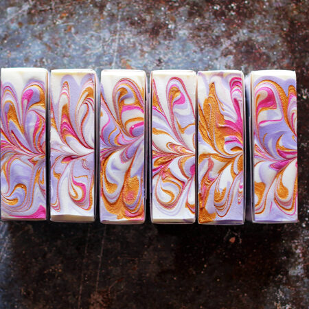 Top down photos of bars of soap, showing swirls of white, purple, pink, and gold mica.
