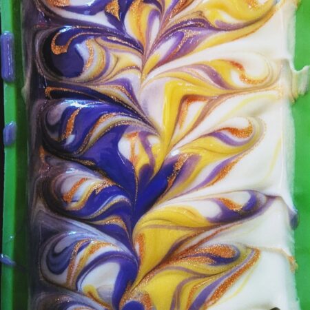 Top down photo of wet soap in a mould. The soap is swirled with purple, yellow, white, and gold.