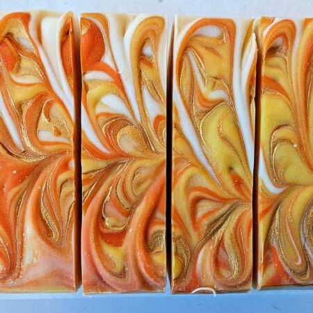 Bars of soap lined up to show their tops. They're brightly swirled with orange, yellow, gold, and hints of white.