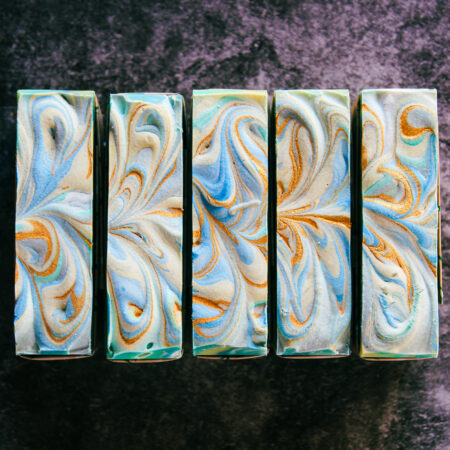 Five bars of soap lined up to show off their tops. They're swirled with green, blue, yellow, white, and gold.