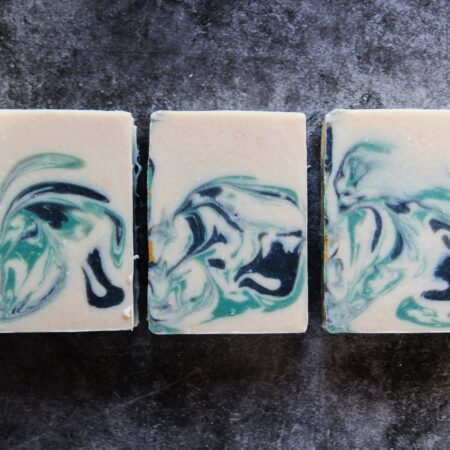 White Soap bars, swirled throughout with green and black. Three bars are laid flat so you can admire the design.