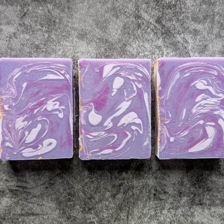 Three purple soaps, with swirls of very pale purple, and brighter pinky purple, flat laid on a stone like background.