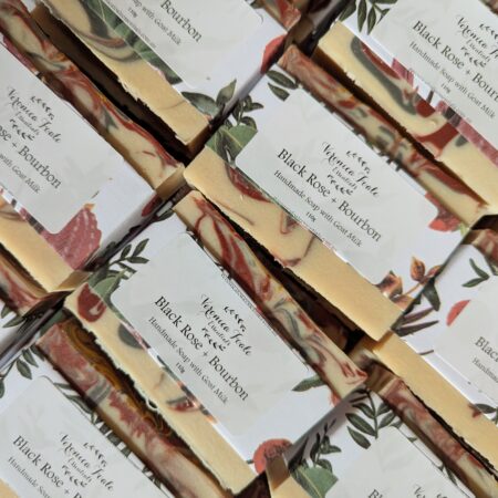 Bars of creamy coloured soap with swirls of deep red and steel grey. They're wrapped in a band of floral paper, with sticker labels on the front.
