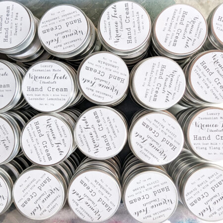 Top Down photo of many aluminium tins with black and white labels. They say Veronica Foale Essentials, Hand Cream, and then the variety.