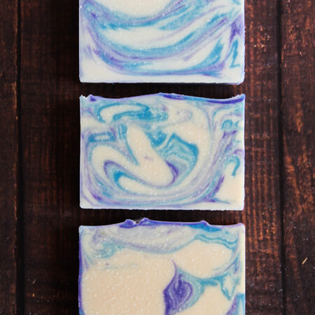 Three bars of soap laid flat against a wood background. The soap is swirled with white, blue, and purple.