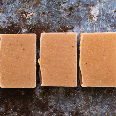 Rich red brown soap bars against an apparent metal background with rust spots. The soap bars are creamy looking, with light speckles of brown.