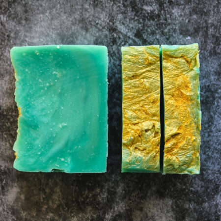 Three bars of soap, set so you can see the top of two, and the surface of another one. The cut surface is almost marbled with green and lighter green - this is an accident. The surface is brushed with gold mica. It isn't as smooth as my bars normally are, but it smells amazing and I love it.