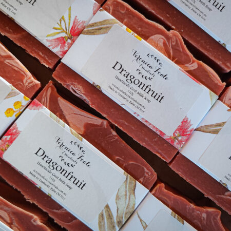 Flat laid bars of soap, with white floral paper as labels. There's a sticker saying "Dragonfruit" and "handmade goat milk soap" with our logo. The bars are a deep red with a lighter swirl through them.